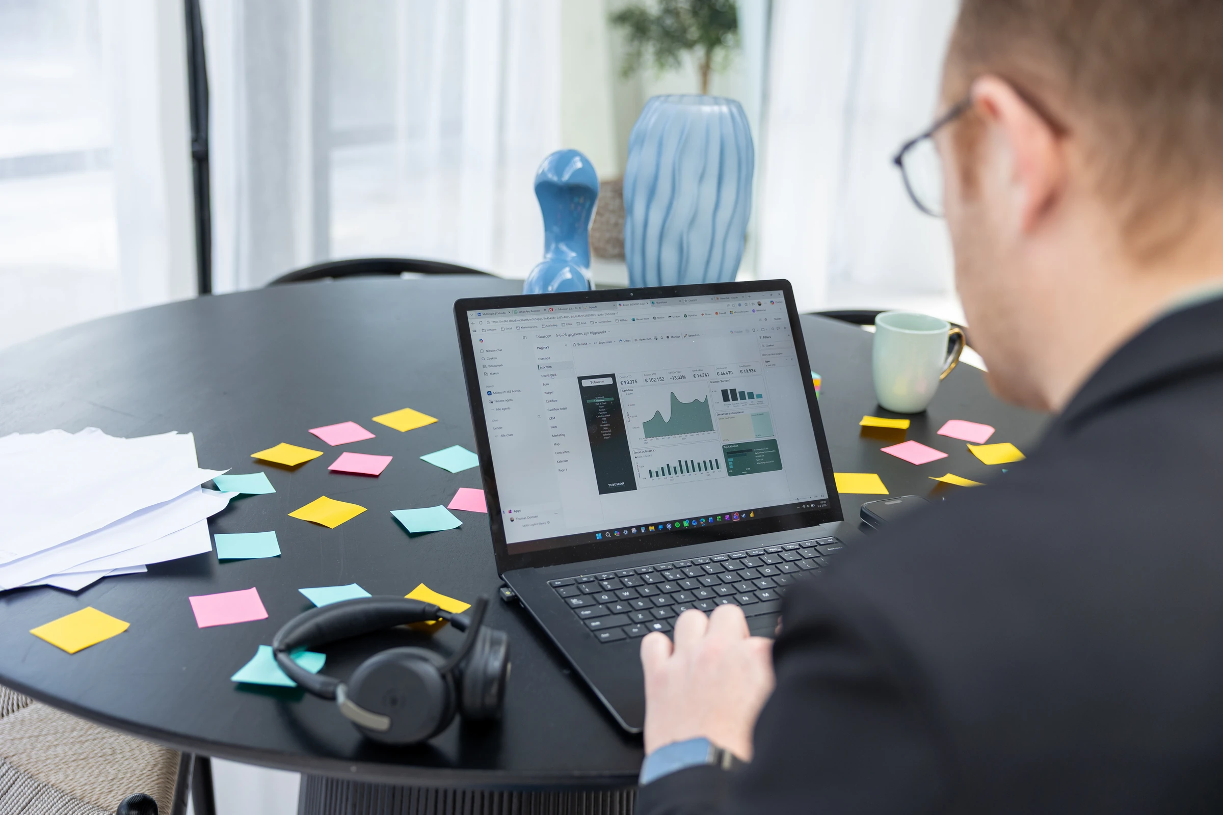 Over de schouder: een dashboard op een laptop, met memobriefjes op tafel