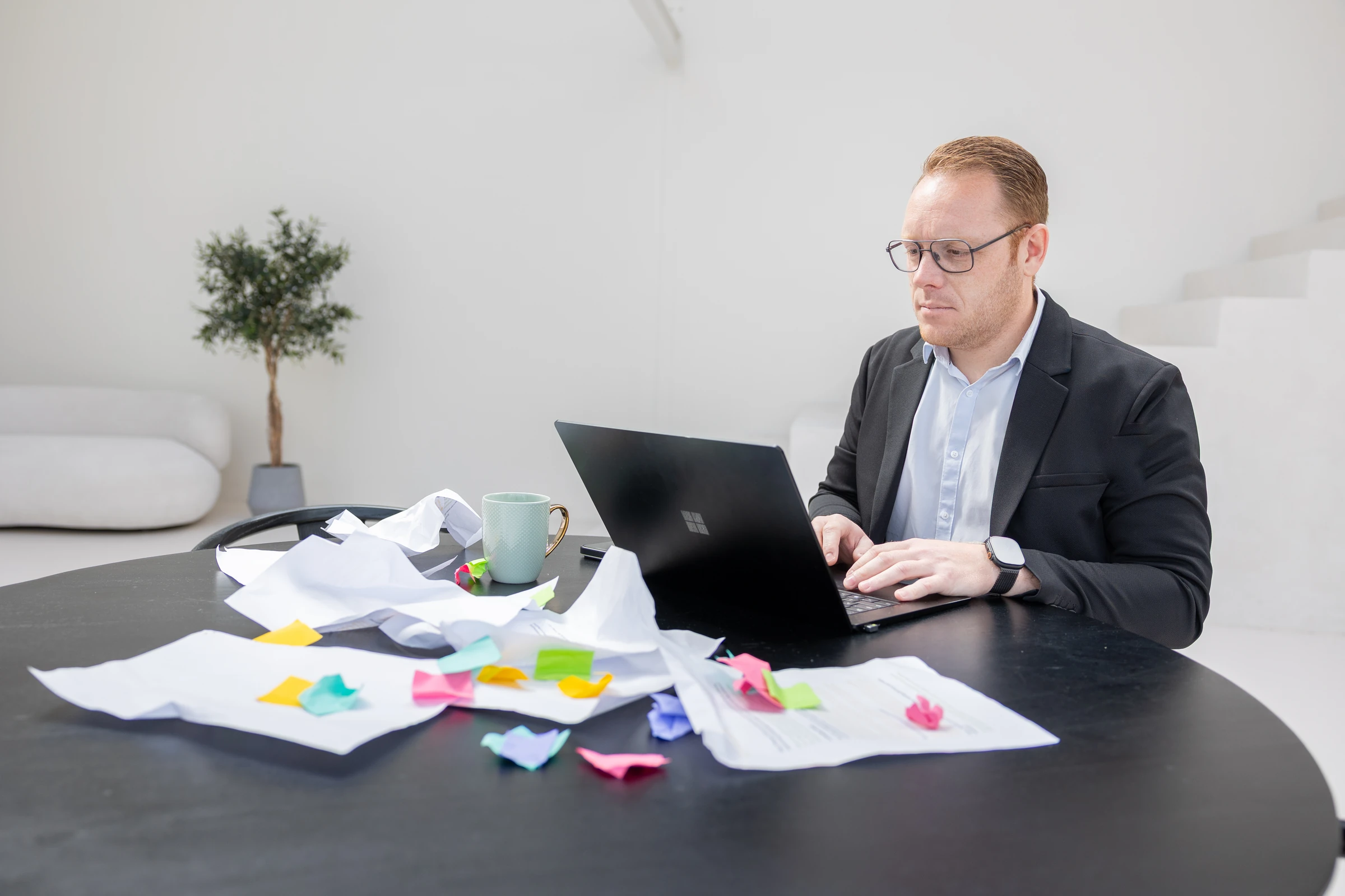Een tafel vol verfrommelde uitdraaien en memobriefjes naast een laptop